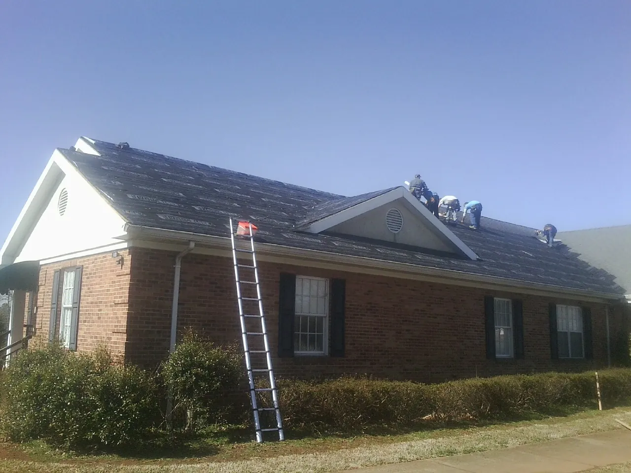Crew tearing shingles off a brick ranch roof with a ladder set — Emergency Roof Repair work by our crew in Millwood