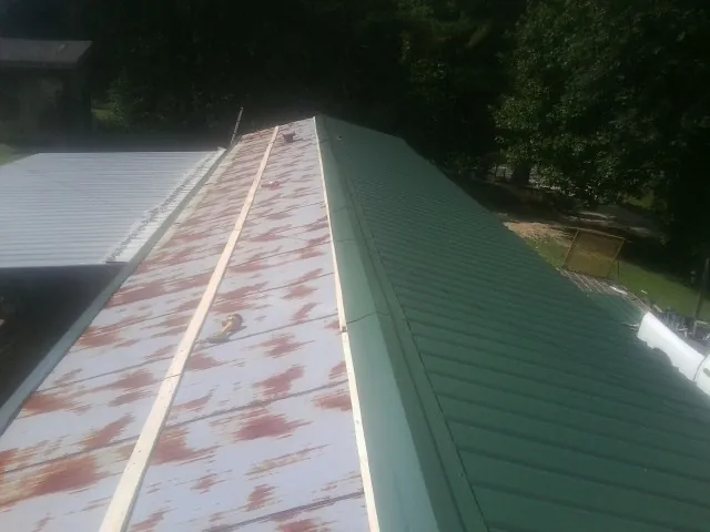 Old rusted panels beside newly installed green metal roofing — Wind Damage Roof Repair by Roofing Brothers in Millwood