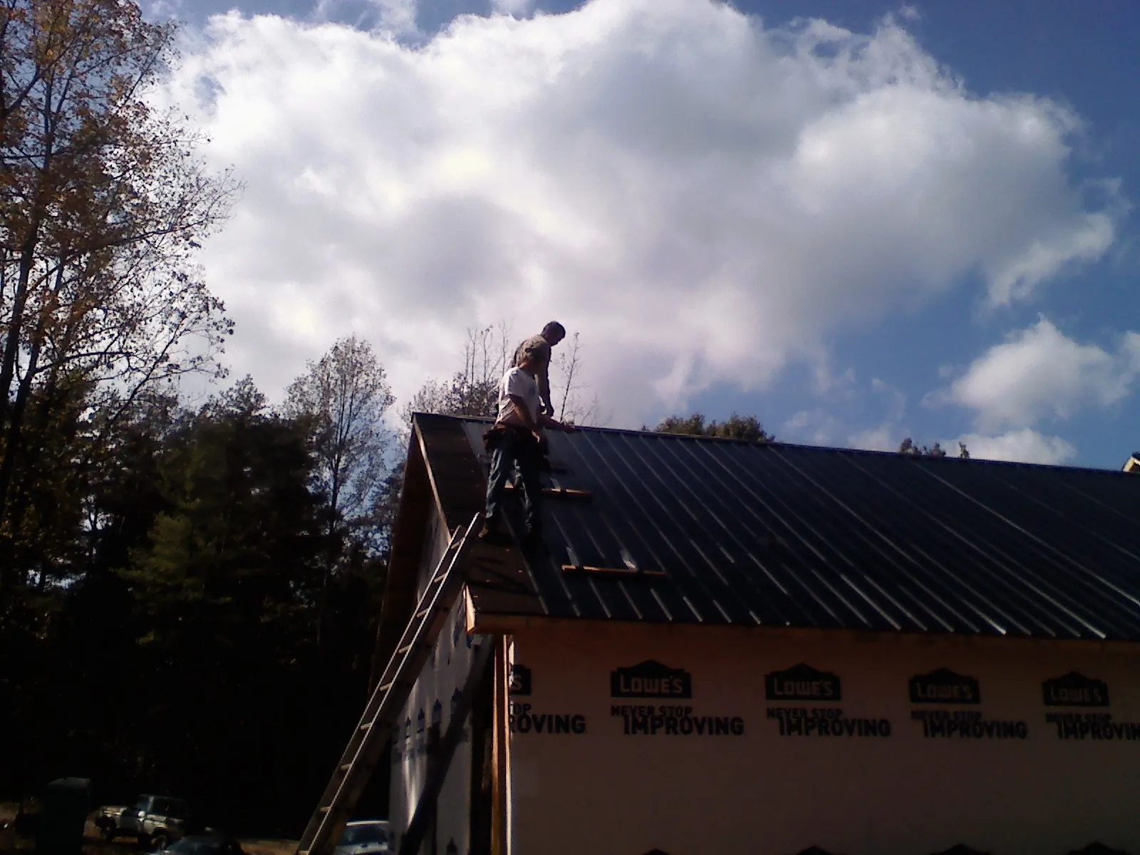 Roofer fastening dark metal panels high against a cloudy sky, from a Roof Inspection job in Millwood